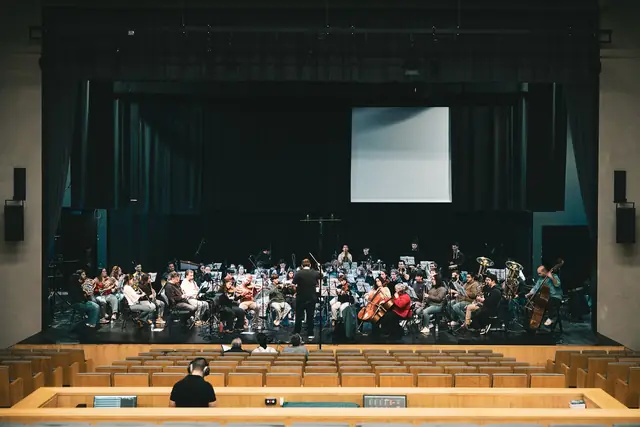 Orquestra em palco num auditório vazio, com microfones em tripés altos